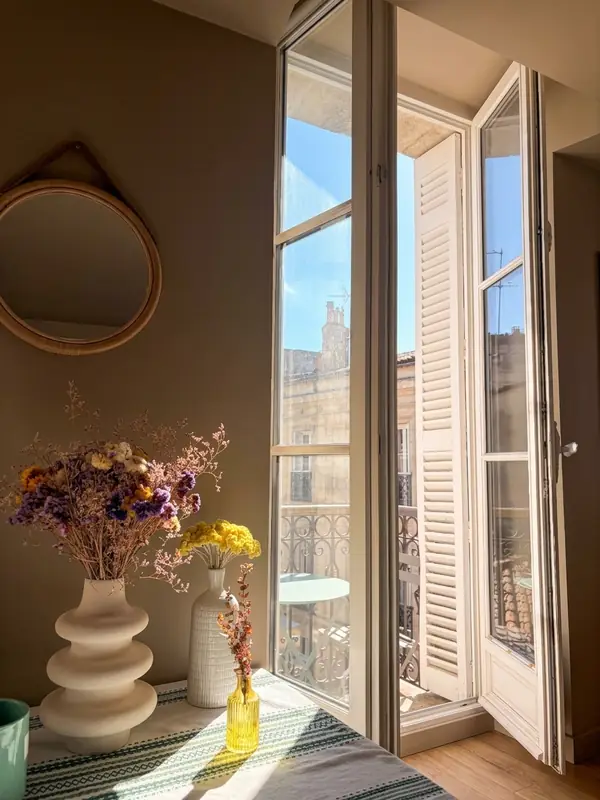 Appartement lumineux à Bordeaux, porte-fenêtre ouverte sur un balcon et bouquet de fleurs séchées