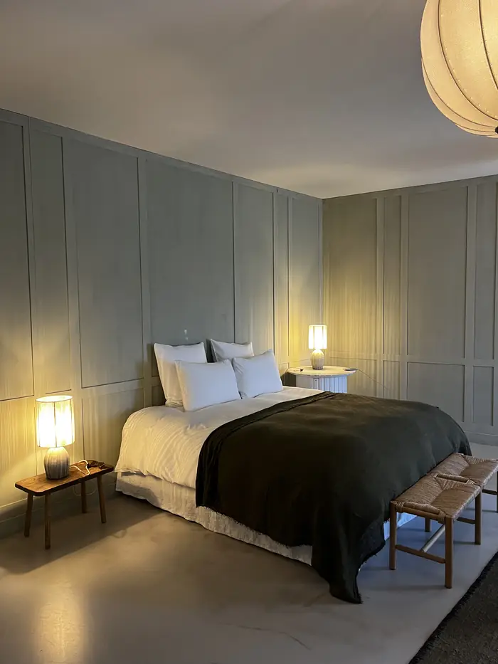 Chambre aux murs vert de gris, lit fait avec plaid foncé et lampes de chevet allumées