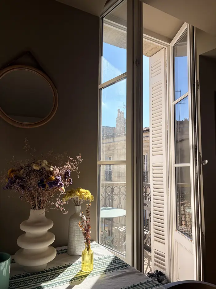 Porte-fenêtre ouverte sur les toits de Bordeaux, vase de fleurs séchées