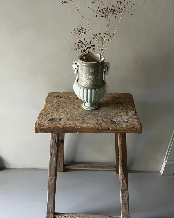 Vase ancien et fleurs séchées posés sur un tabouret en bois brut